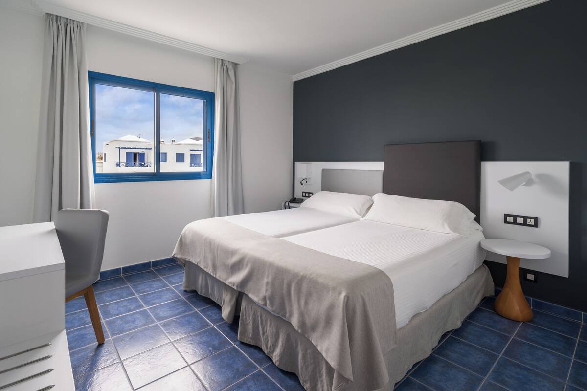 A hotel room with a large bed, a desk, and a view of buildings outside the window.