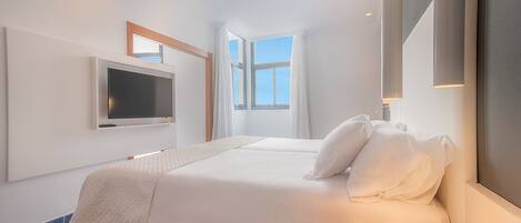 Une chambre d’hôtel moderne dotée d’un grand lit, d’un téléviseur à écran plat fixé au mur et d’une grande fenêtre laissant entrer la lumière naturelle.