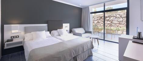 A modern hotel room with two beds, a desk, and a balcony with a stone wall view.