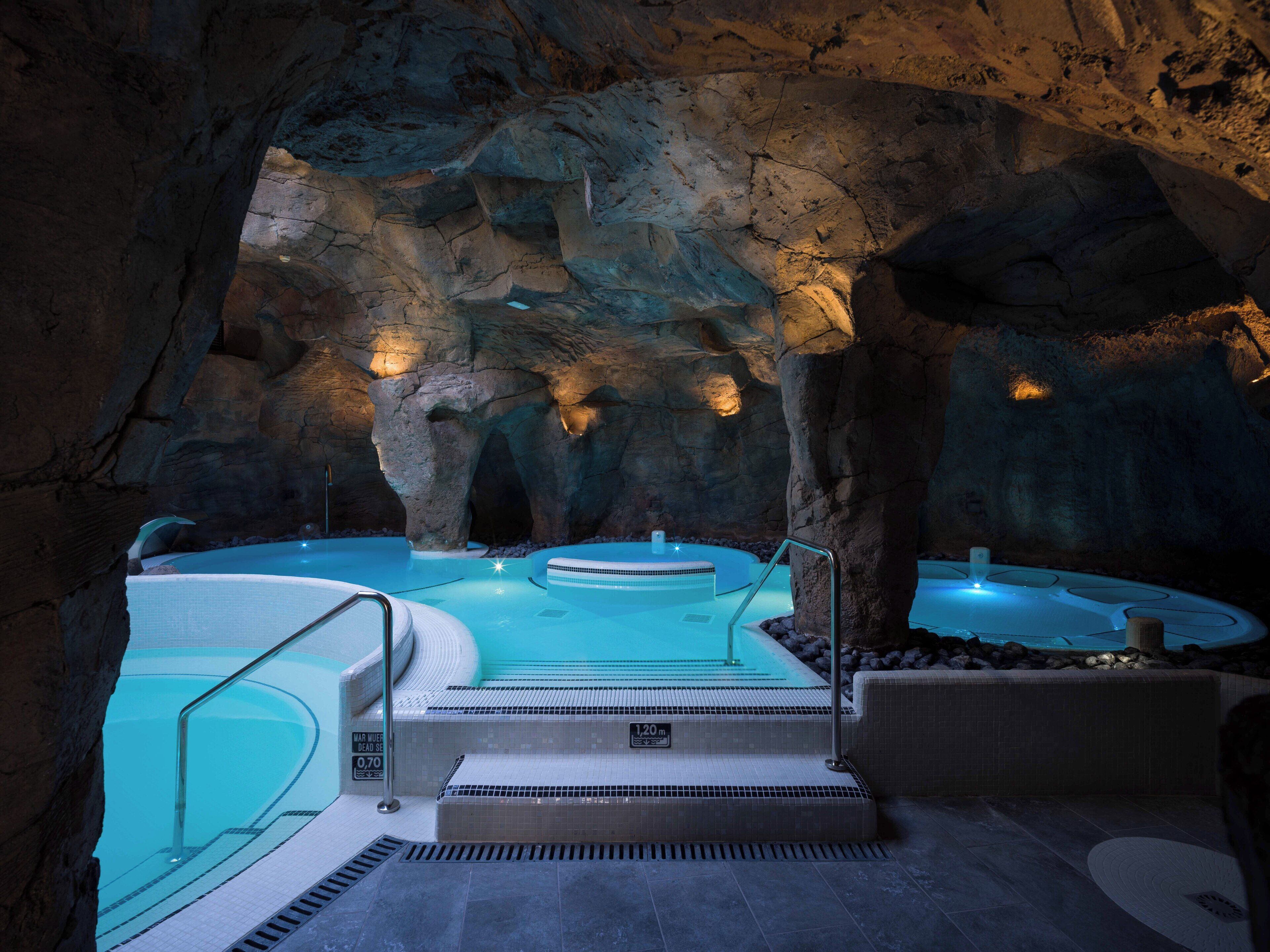 A spa area with multiple hot tubs set in a cave-like environment, featuring stone walls and lighting.