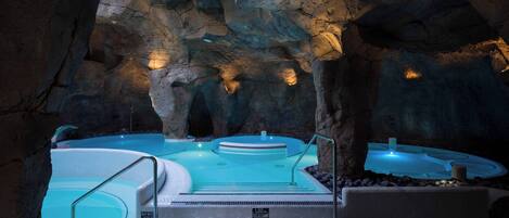 A spa area with multiple hot tubs set in a cave-like environment, featuring stone walls and lighting.