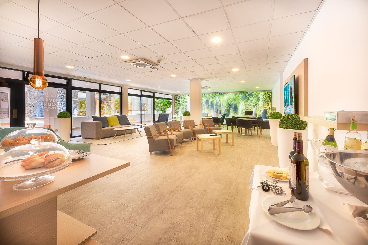 A modern hotel lobby with seating areas, a reception desk, and a dining setup with a wine bottle and glasses.