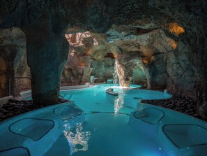 Une piscine intérieure aménagée dans une grotte naturelle, avec une fontaine centrale et plusieurs espaces de détente.