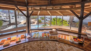 Un espace buffet proposant une variété de plats et offrant une vue sur la piscine et les bâtiments du complexe.