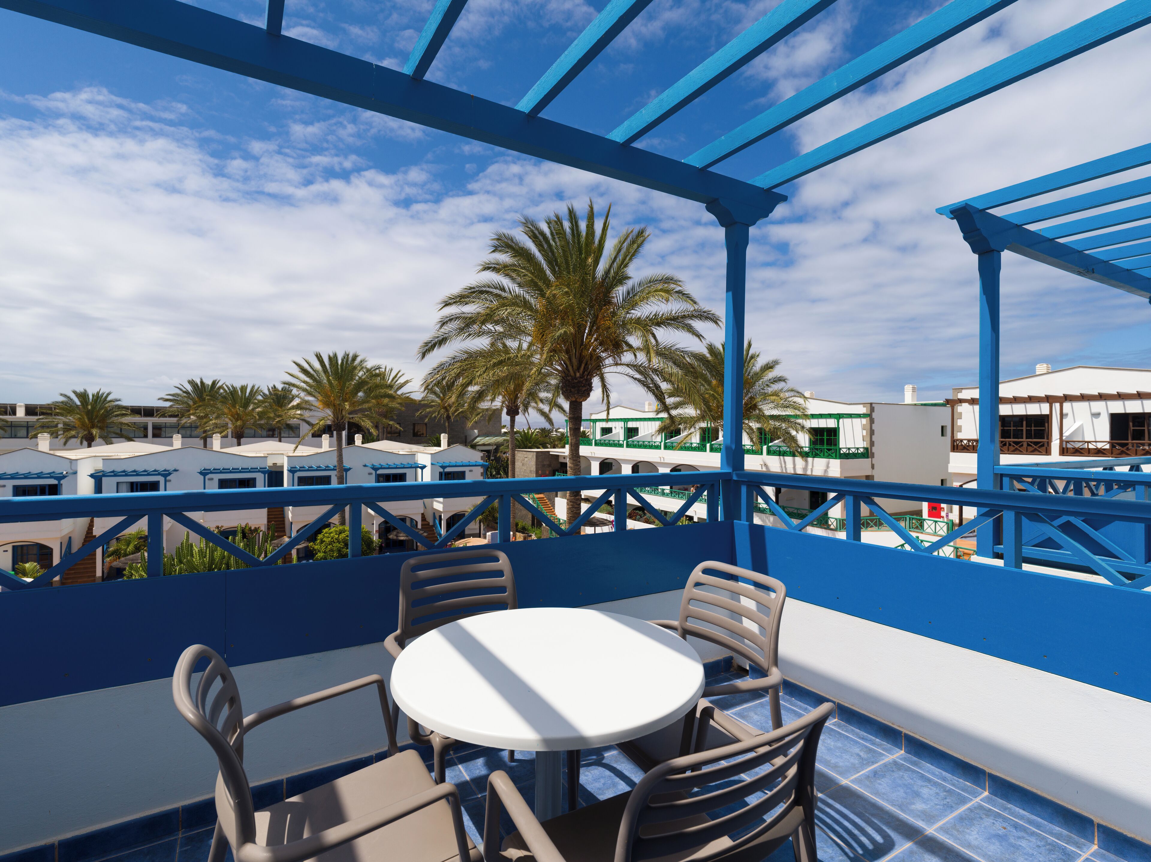 A covered outdoor seating area with a table and chairs, overlooking a pool and palm trees.