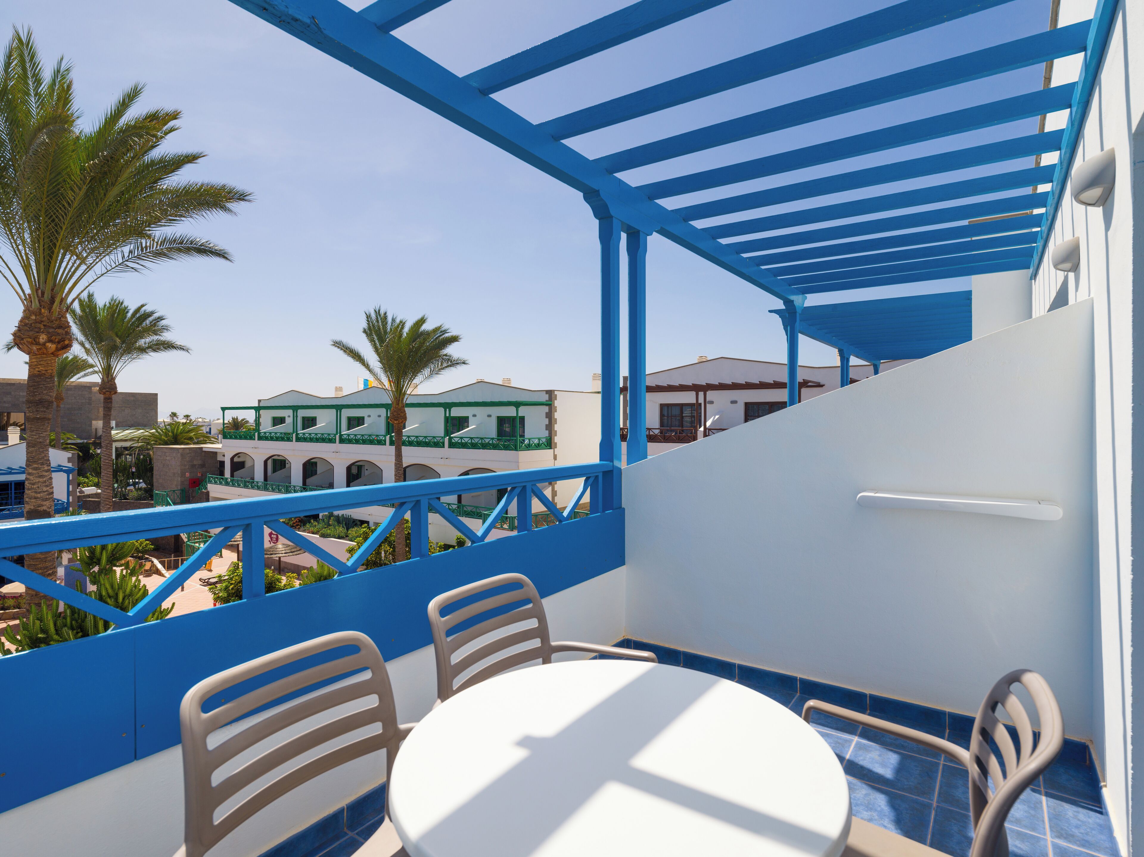 A balcony with a white table and chairs, overlooking a pool and palm trees.