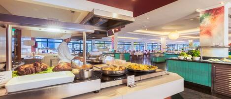 A buffet area with various food items, a chef preparing food, and a seating area in the background.