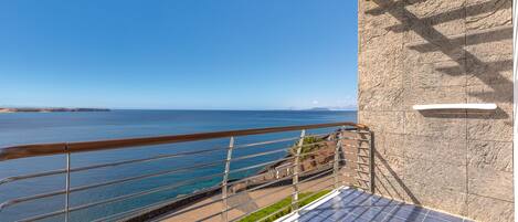 A balcony with a view of the sea, a stone wall, and a small table with a chair.