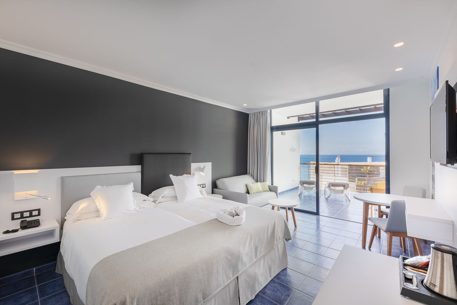Una camera d'albergo moderna con un letto grande, una scrivania e un balcone vista mare.