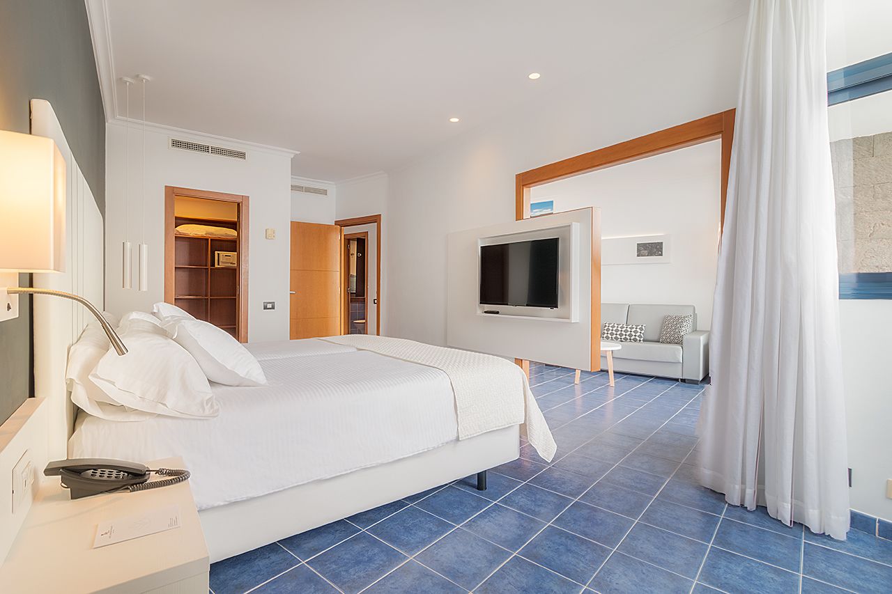 Habitación de hotel con cama, televisor, escritorio con teléfono, armario y puerta al baño.