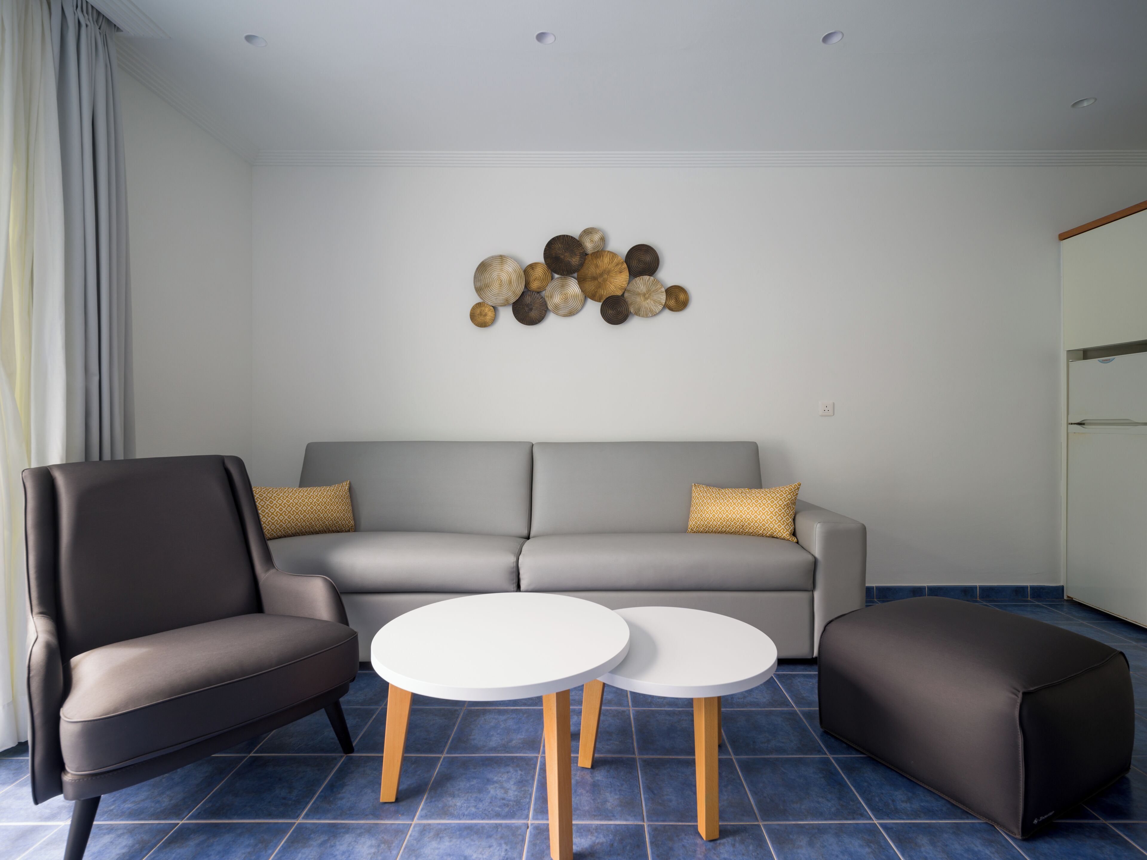 A modern living room with a grey sofa, two white round tables, and a decorative wall piece.