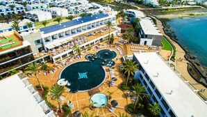 Vue aérienne d’un complexe hôtelier doté de plusieurs piscines, de chaises longues et d’une zone de plage.