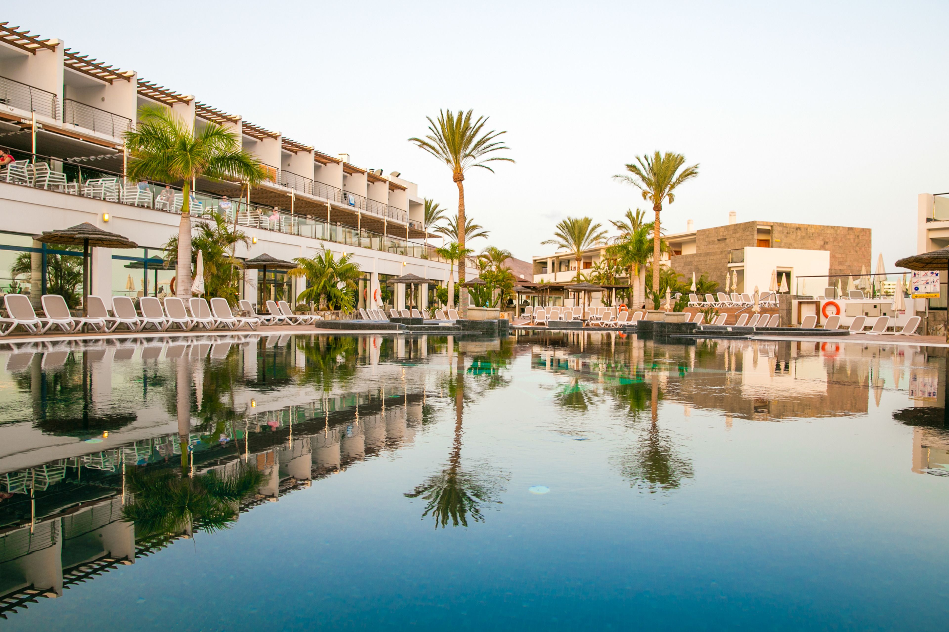 A pool area with lounge chairs and palm trees, surrounded by buildings with balconies and outdoor seating.