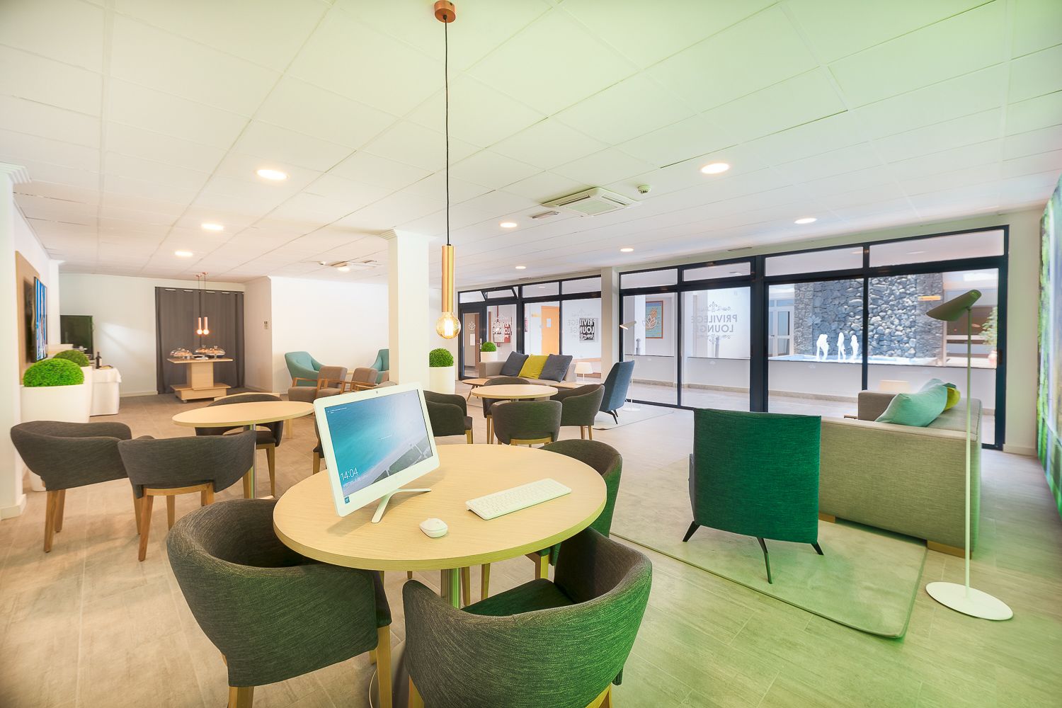 Un espace de bureau moderne avec des tables rondes, des chaises vertes et une grande fenêtre donnant sur l’extérieur.