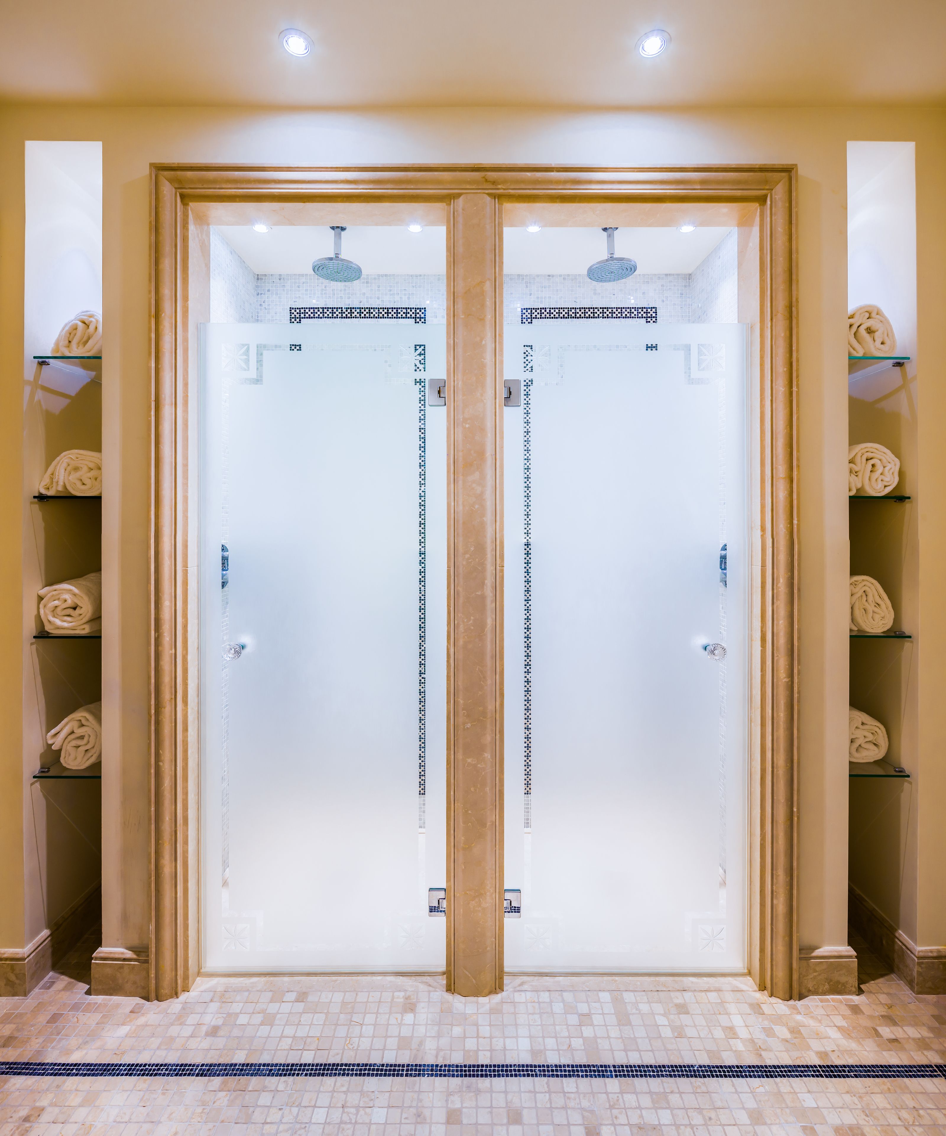 Un bagno con specchio, pavimento piastrellato, una colonna centrale e ripiani per asciugamani su entrambi i lati.