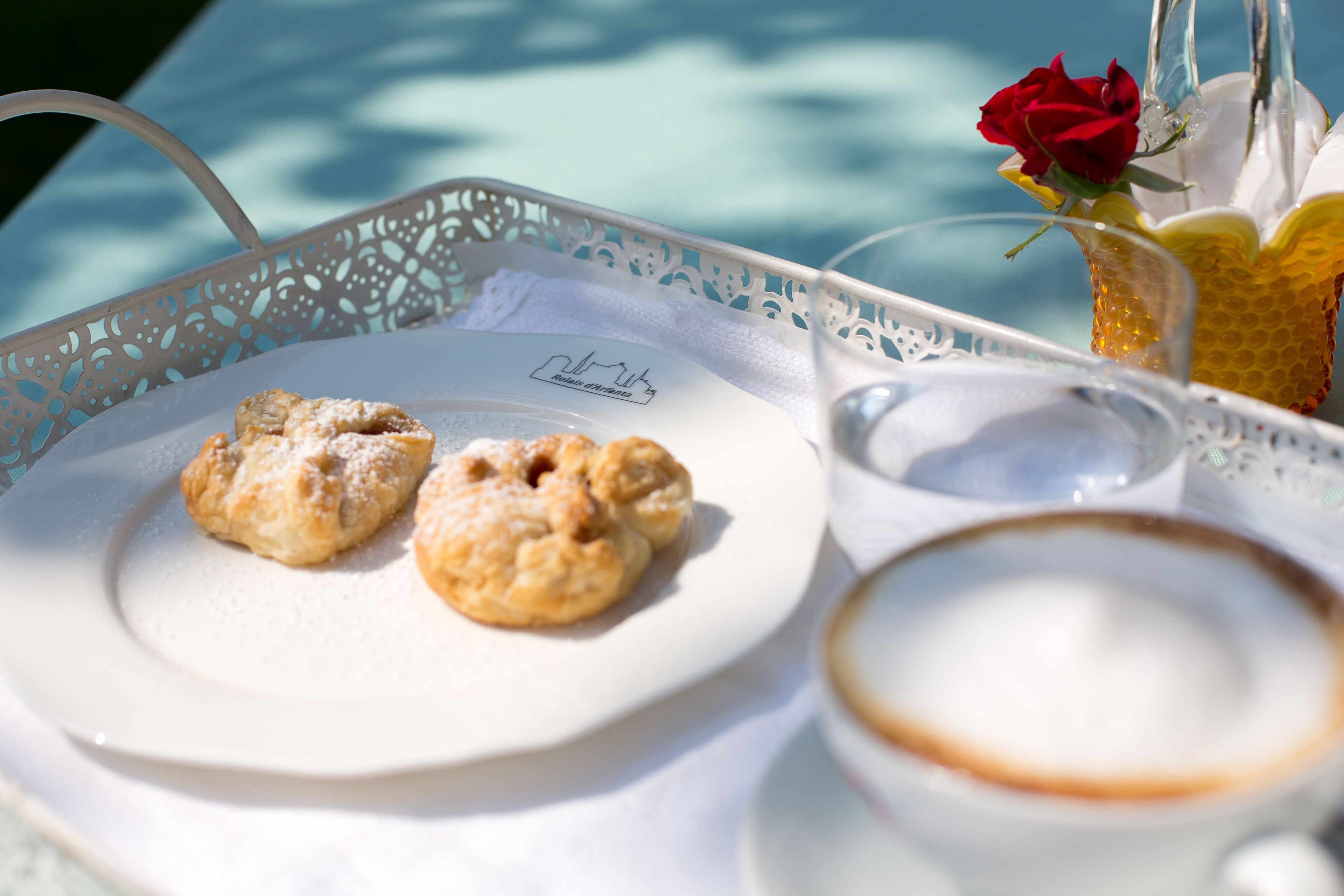 A tray with pastries and a cup of coffee, a rose in a glass, and a menu on a table.