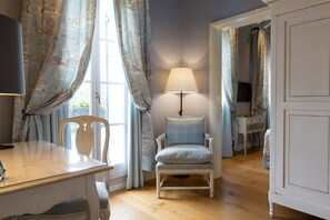 Una habitación con piso de madera, una silla blanca, una mesa, una lámpara y un armario.