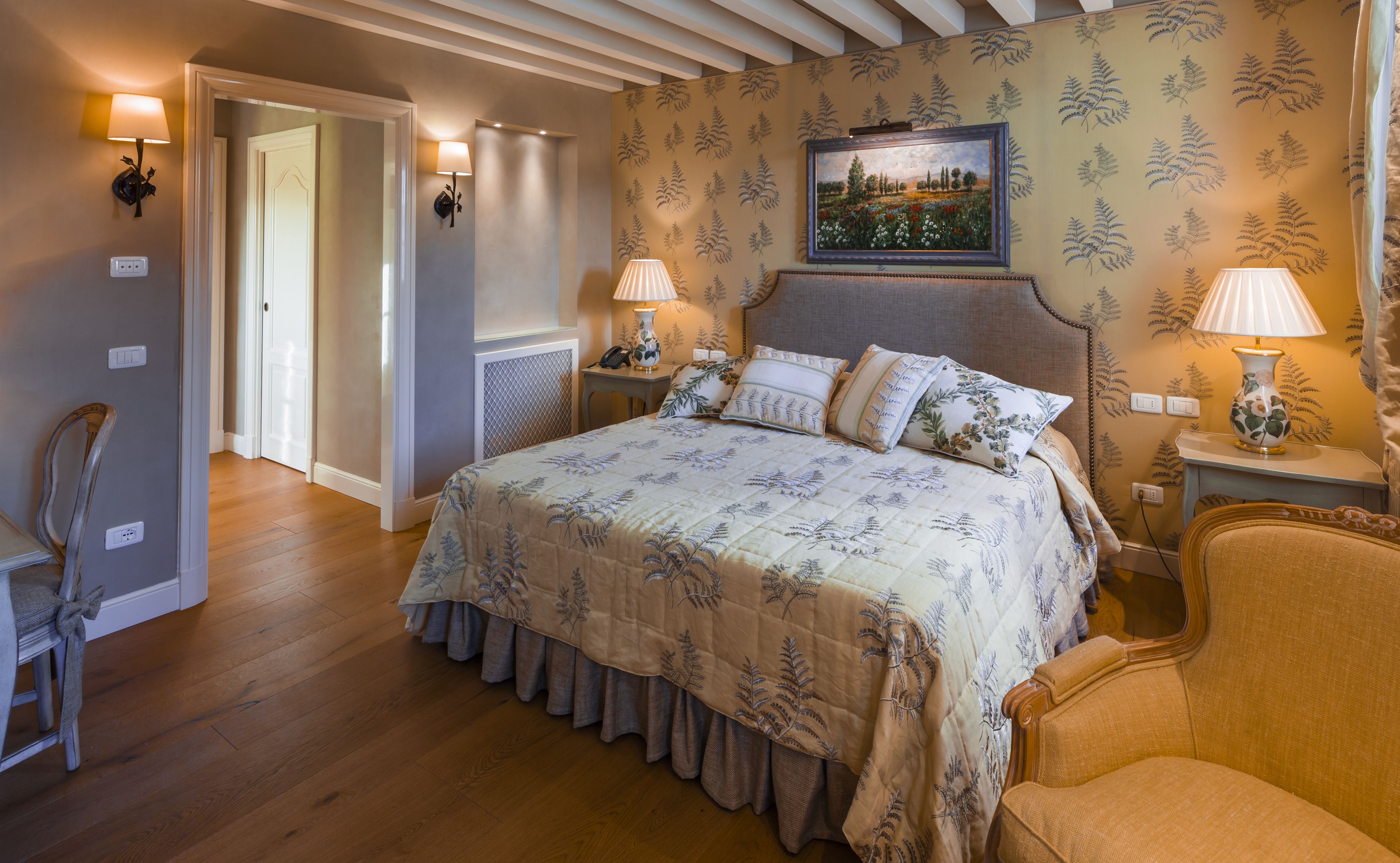 Un dormitorio con una cama grande, dos lámparas de noche, una mesita de noche, una silla y un cuadro en la pared.