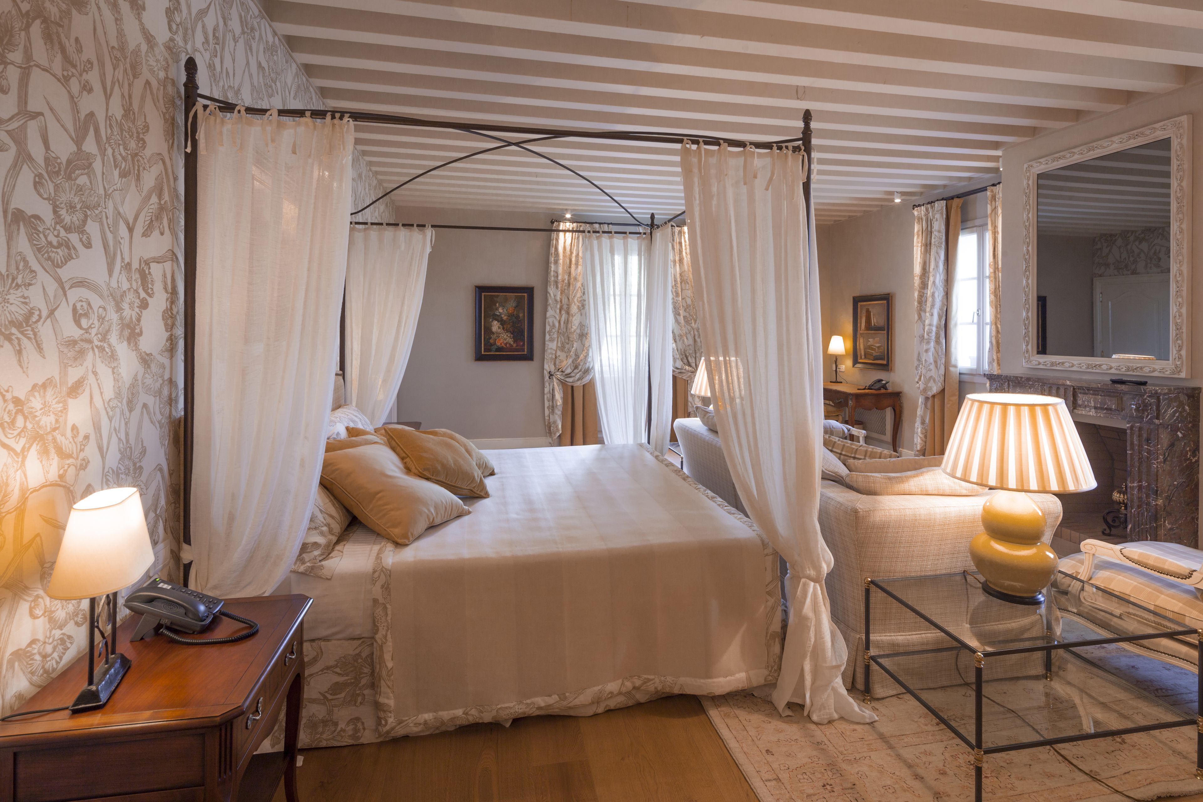 Un dormitorio con cama con dosel, una mesita de noche con lámpara, una silla y una pequeña mesa con lámpara.