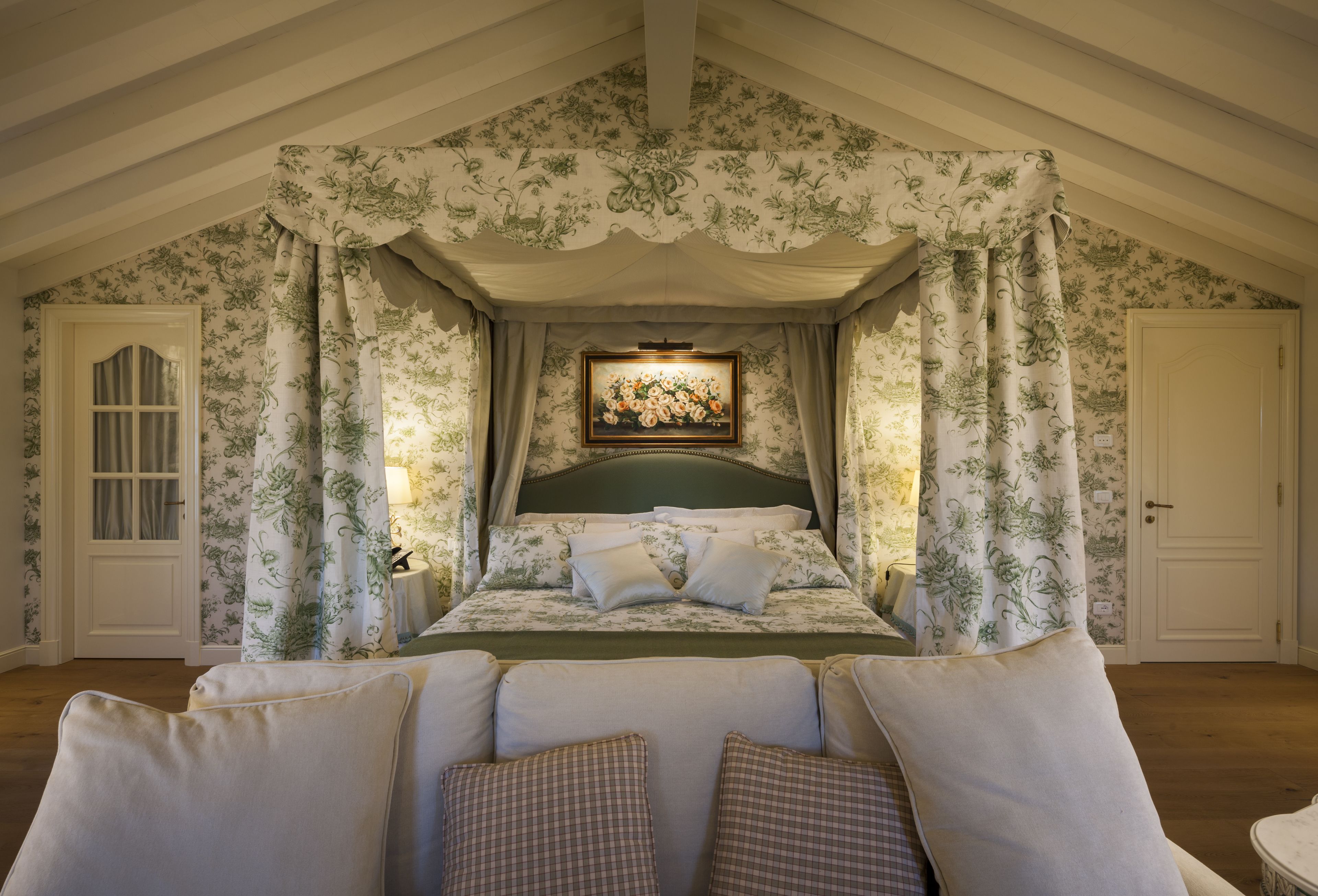 Un dormitorio con cama con dosel, papel tapiz floral y un cuadro enmarcado sobre la cama.