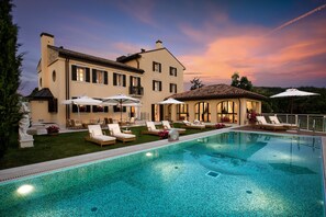 A large pool with lounge chairs and umbrellas, a well-maintained lawn, and a building with multiple windows and a balcony. - Relais d'Arfanta (Tarzo)