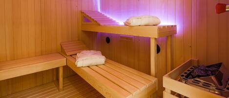 A sauna room with wooden benches, a bench with towels, and a wooden bucket.