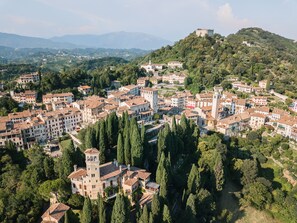 Vista aérea de un pueblo histórico con un castillo destacado en una colina, rodeado de abundante vegetación y arquitectura tradicional.
