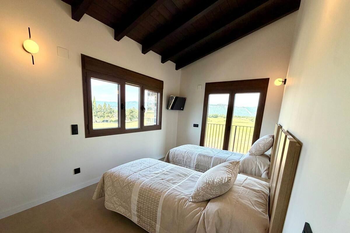 A bedroom with two beds, large windows, a TV, and a balcony.