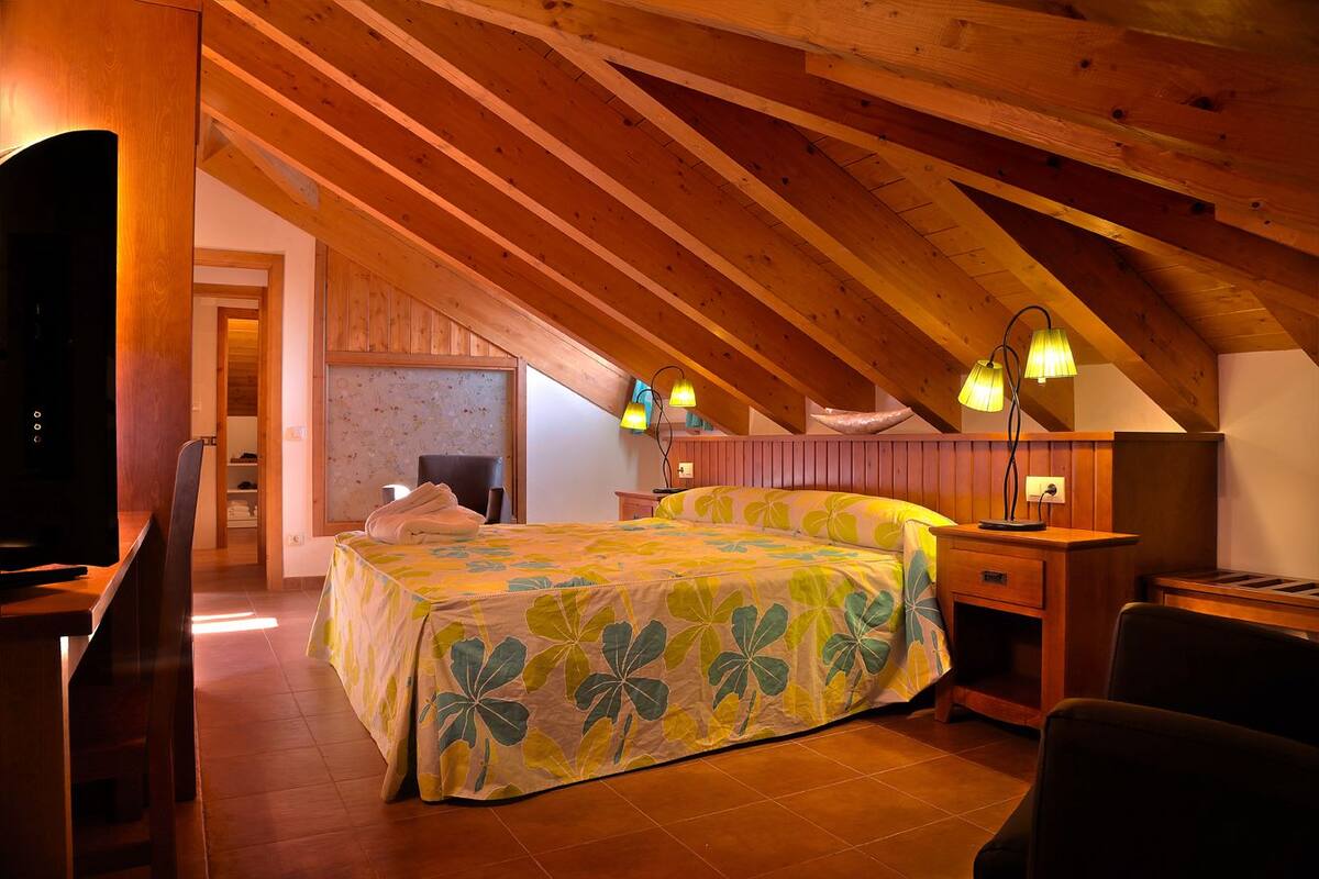 A cozy attic bedroom with a bed, wooden beams, and a television.