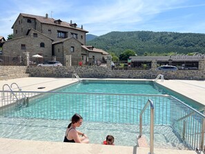 A swimming pool with stone buildings in the background. - Casas Pirineo Aínsa: Pool & Garden (Ainsa)