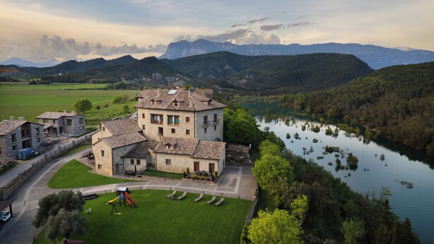 Un gran edificio de piedra con un patio interior, rodeado de abundante vegetación y un lago.