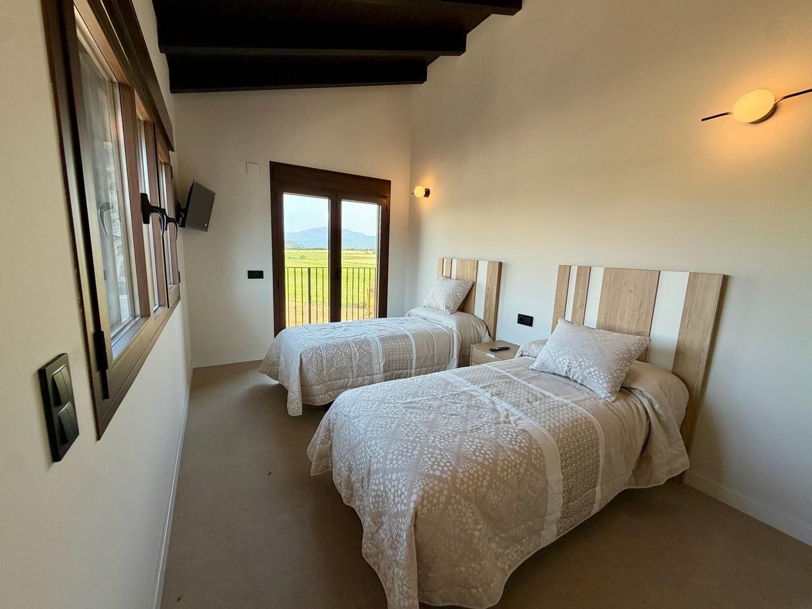 A bedroom with two beds, a balcony, and a TV mounted on the wall.