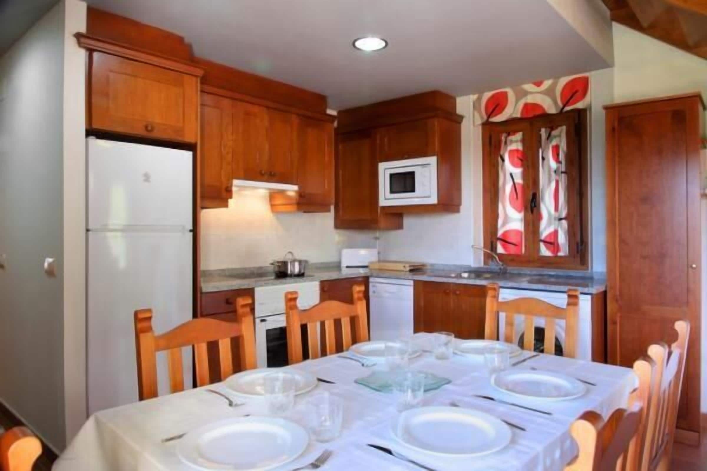 A compact kitchen with wooden cabinets, a microwave, and a dining table set for four.