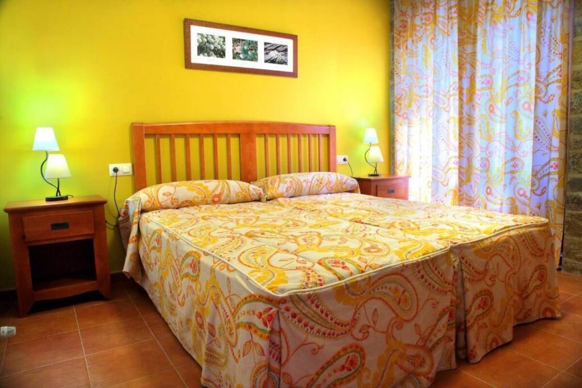 A bedroom with a bed, two bedside tables, a nightstand, a wall-mounted picture, and a patterned curtain.