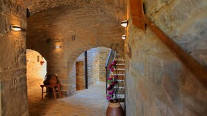 Un corredor de piedra con arcos, una silla de madera, un jarrón con flores e iluminación empotrada en las paredes.