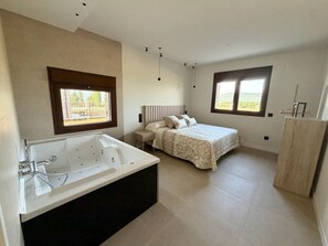 A modern bedroom with a large bed, a separate bathroom with a bathtub, and two windows providing natural light.