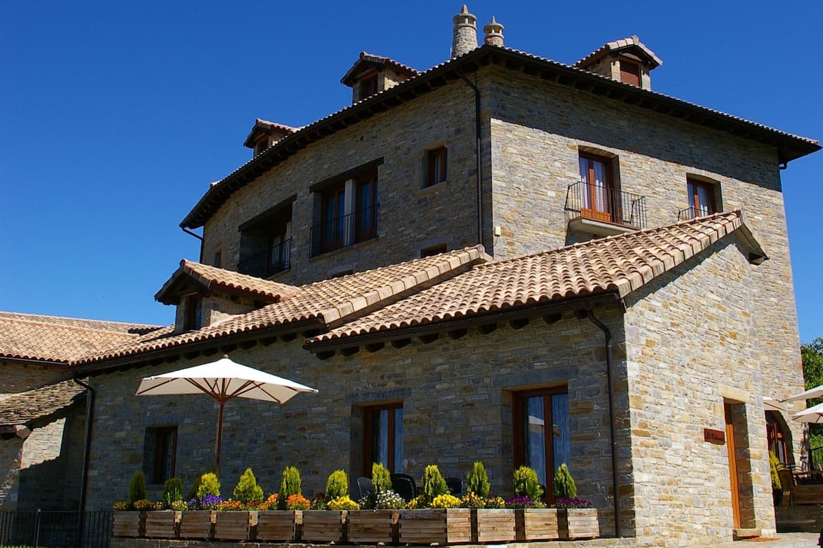 A stone building with a tiled roof, multiple windows, and a balcony.