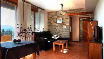 Una sala de estar con un sofá negro, una mesa de centro de madera y una pared de piedra.