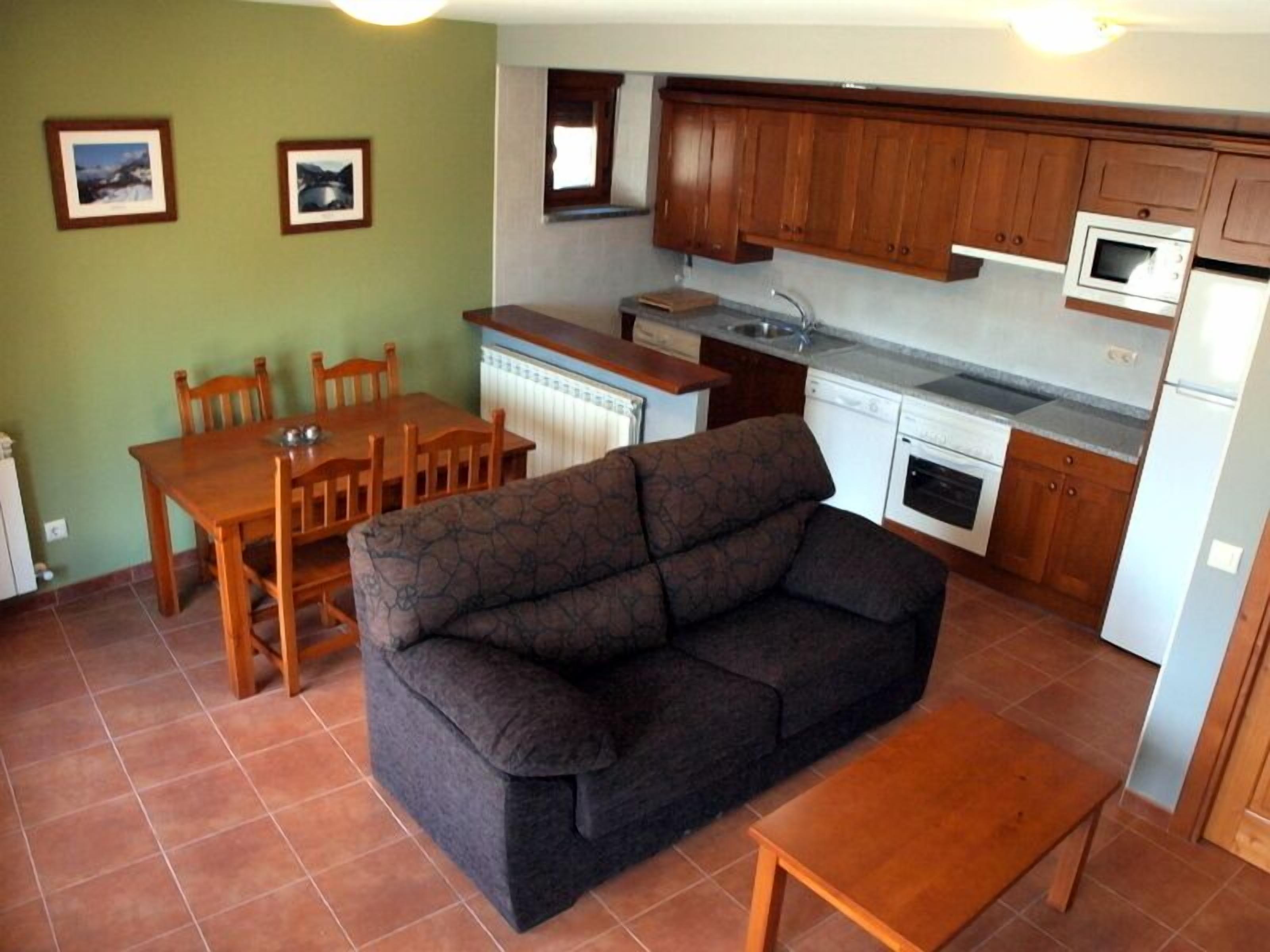 Un espacio habitable compacto con sofá, mesa de comedor, sillas, kitchenette y dos cuadros en la pared.