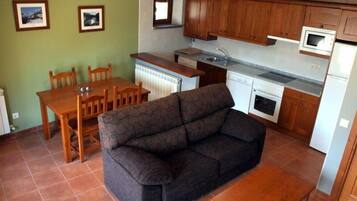 Un espacio habitable compacto con sofá, mesa de comedor, sillas, kitchenette y dos cuadros en la pared.