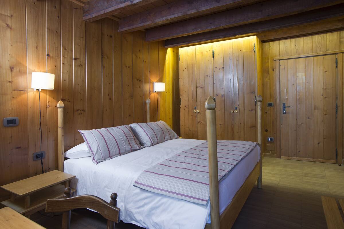 A wooden room with a bed, bedside lamps, and a wooden bench.