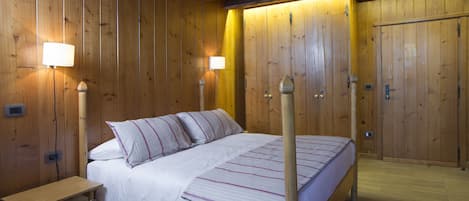 A wooden room with a bed, bedside lamps, and a wooden bench.