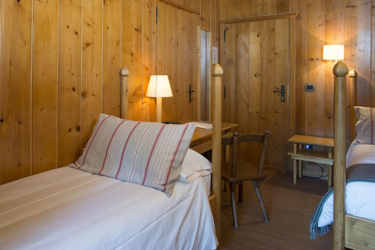 A wooden room with a bed, a chair, a desk, and a lamp.