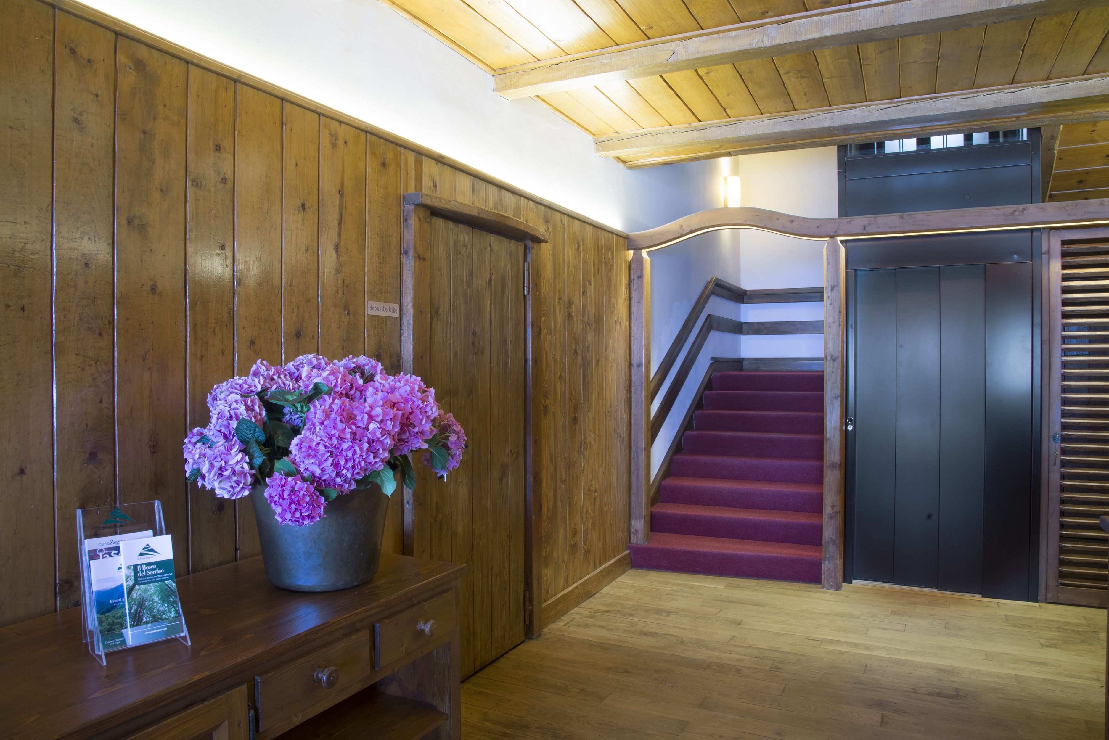 Un interno in legno con una scala, una scrivania di legno con un vaso di fiori e un espositore per brochure.
