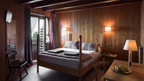 Ein Zimmer mit Holzwandverkleidung, einem Bett, Nachttischlampen, einem Schreibtisch mit Lampe und einem Sessel.