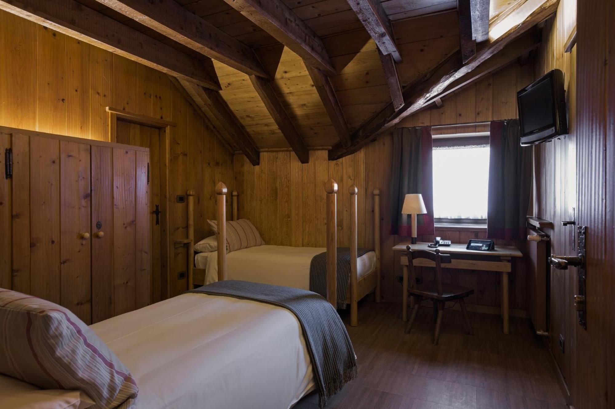 Ein Zimmer in einer Holzhütte mit zwei Betten, einem Schreibtisch, einem Stuhl und einem Fernseher.