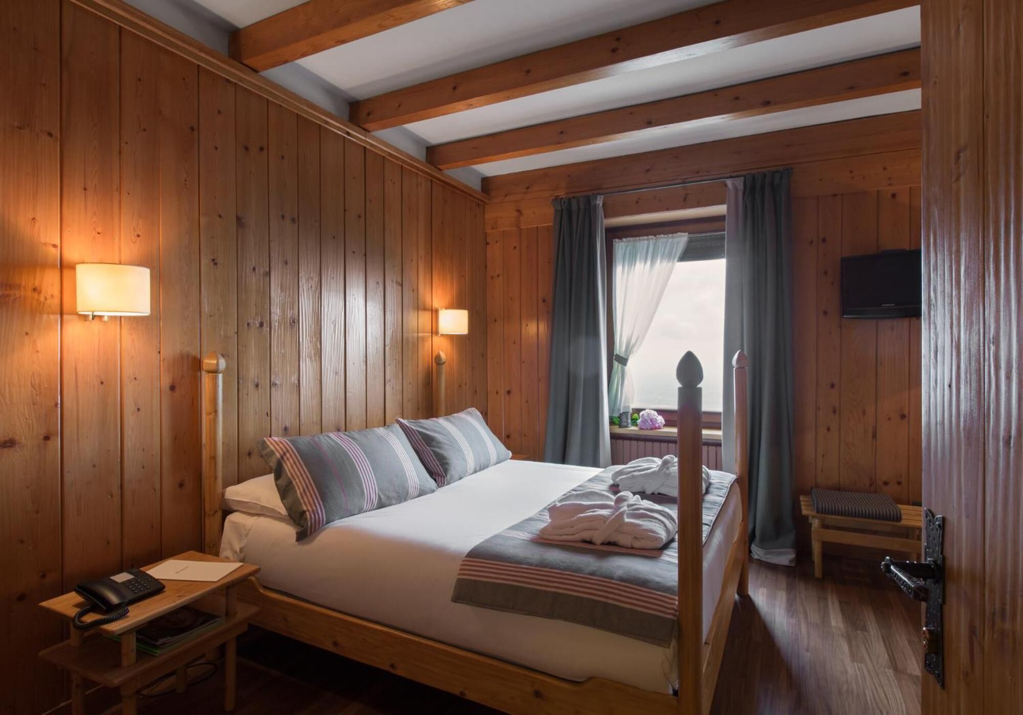 A wooden-paneled room with a bed, bedside lamps, a telephone, and a television.