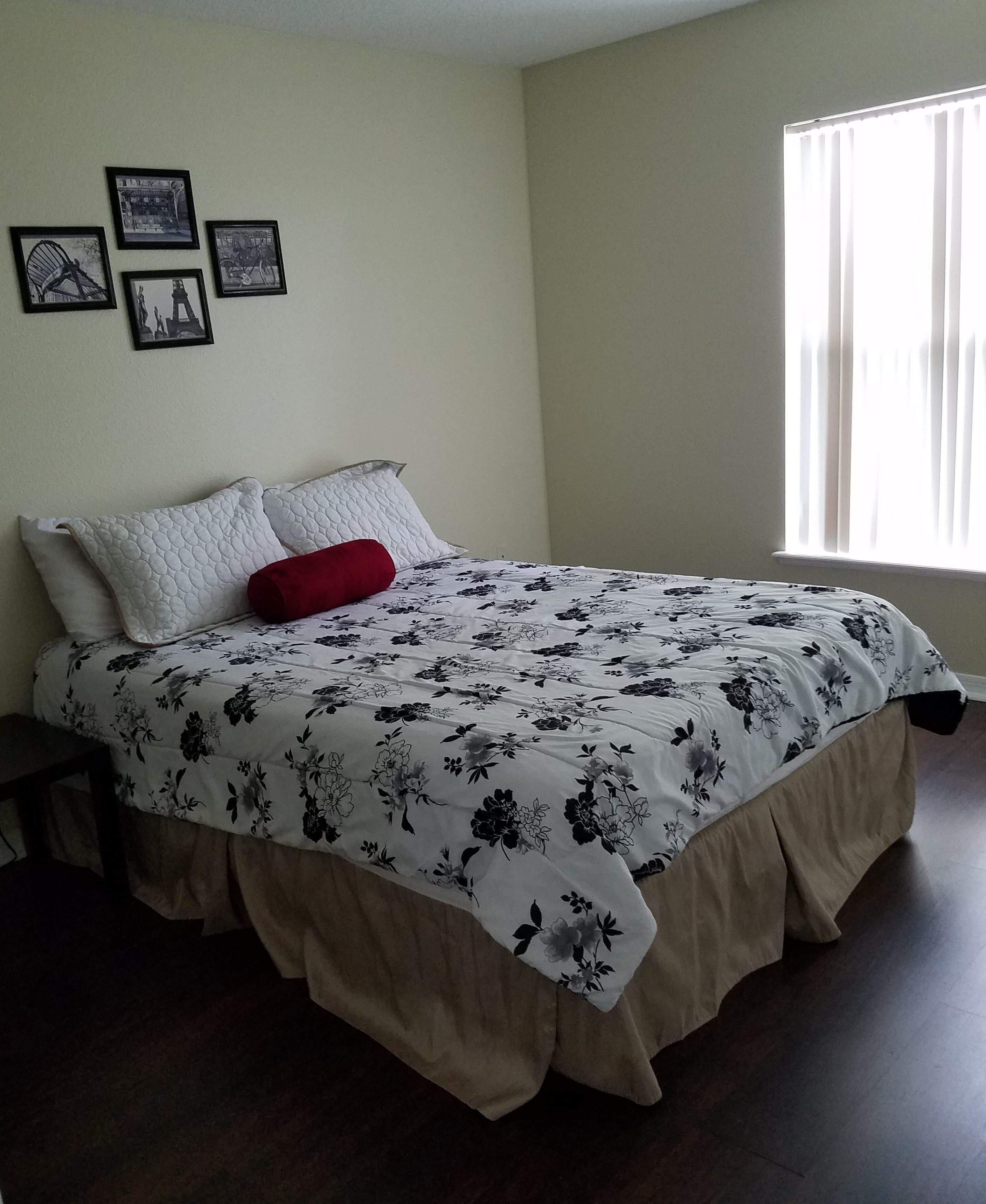 Quarto com cama, mesa de cabeceira e janela com cortinas.