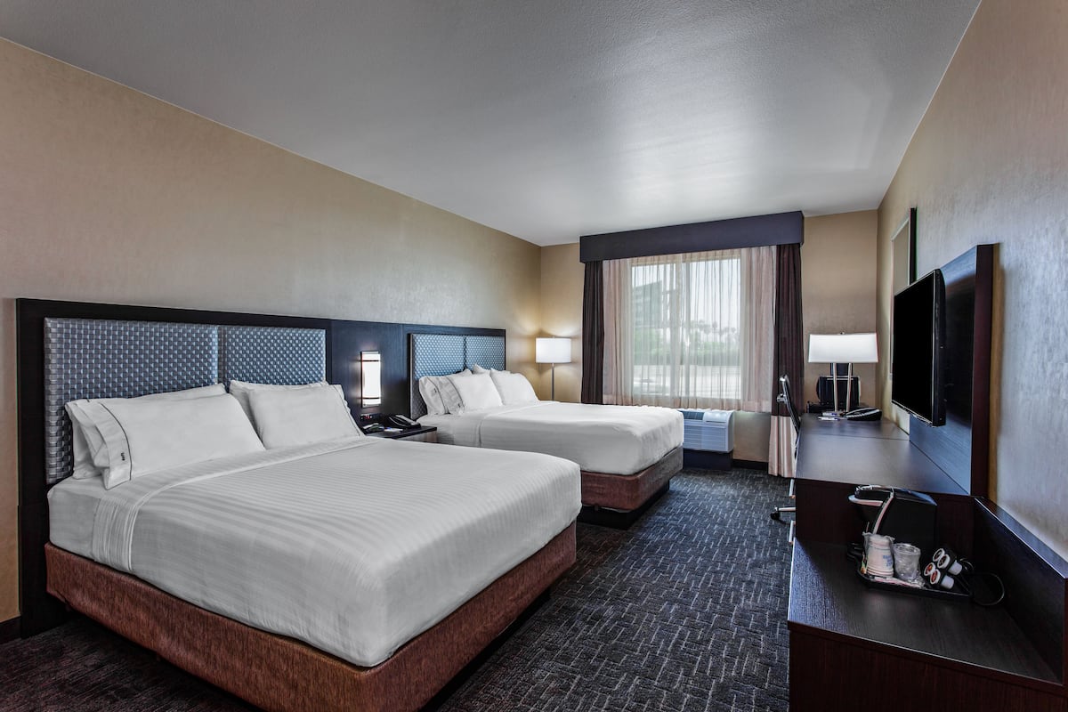 A hotel room with two beds, a desk, a TV, and a window with curtains.