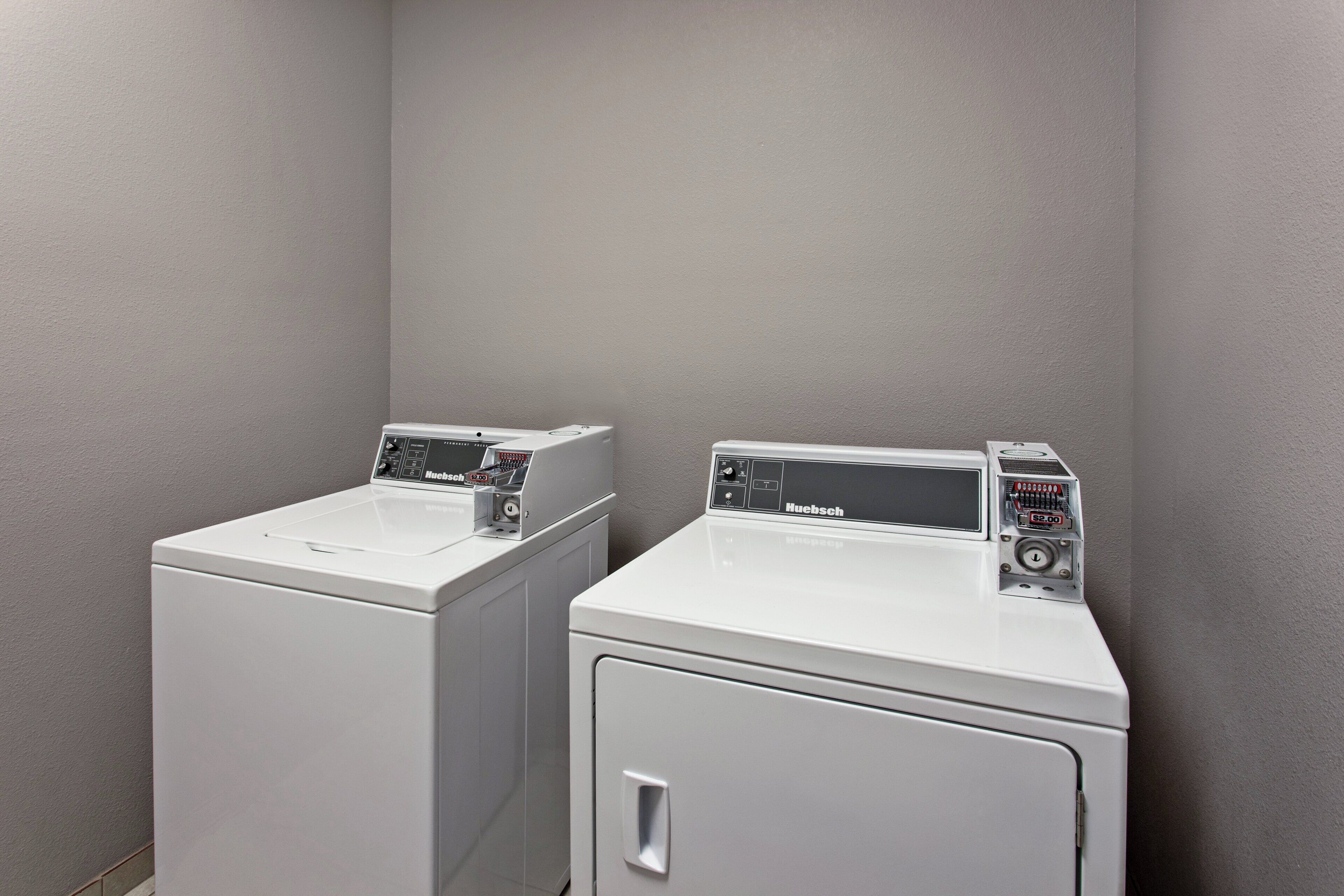 Two front-loading white washing machines in a corner with grey walls.